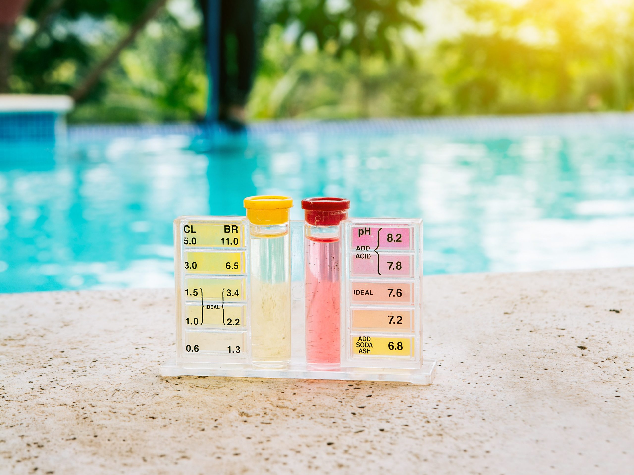 water ph tester kit on the edge of the swimming pool with maintenance person in the background photo