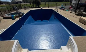 An empty blue swimming pool with white steps and concrete surround, under a clear blue sky.